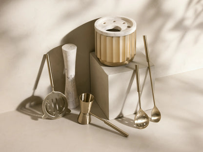 Close-up of brushed gold Dayan Bar Tools: strainer, spoon, jigger, and marble muddler in a ribbed gold holder.