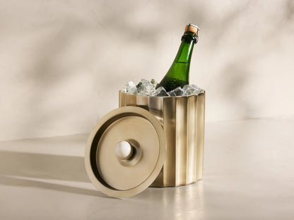 Fluted brass Dayana Ice Bucket holding a green champagne bottle with ice. Its lid, with a white marble handle, rests beside it.