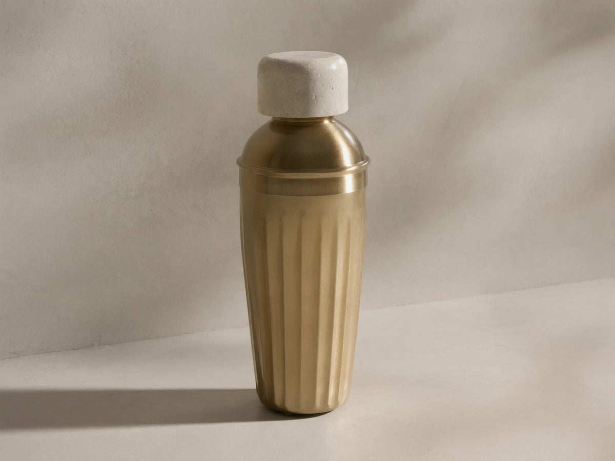 Front view of the Dayana Cocktail Shaker, featuring a light marble cap and a fluted brass-finished body.