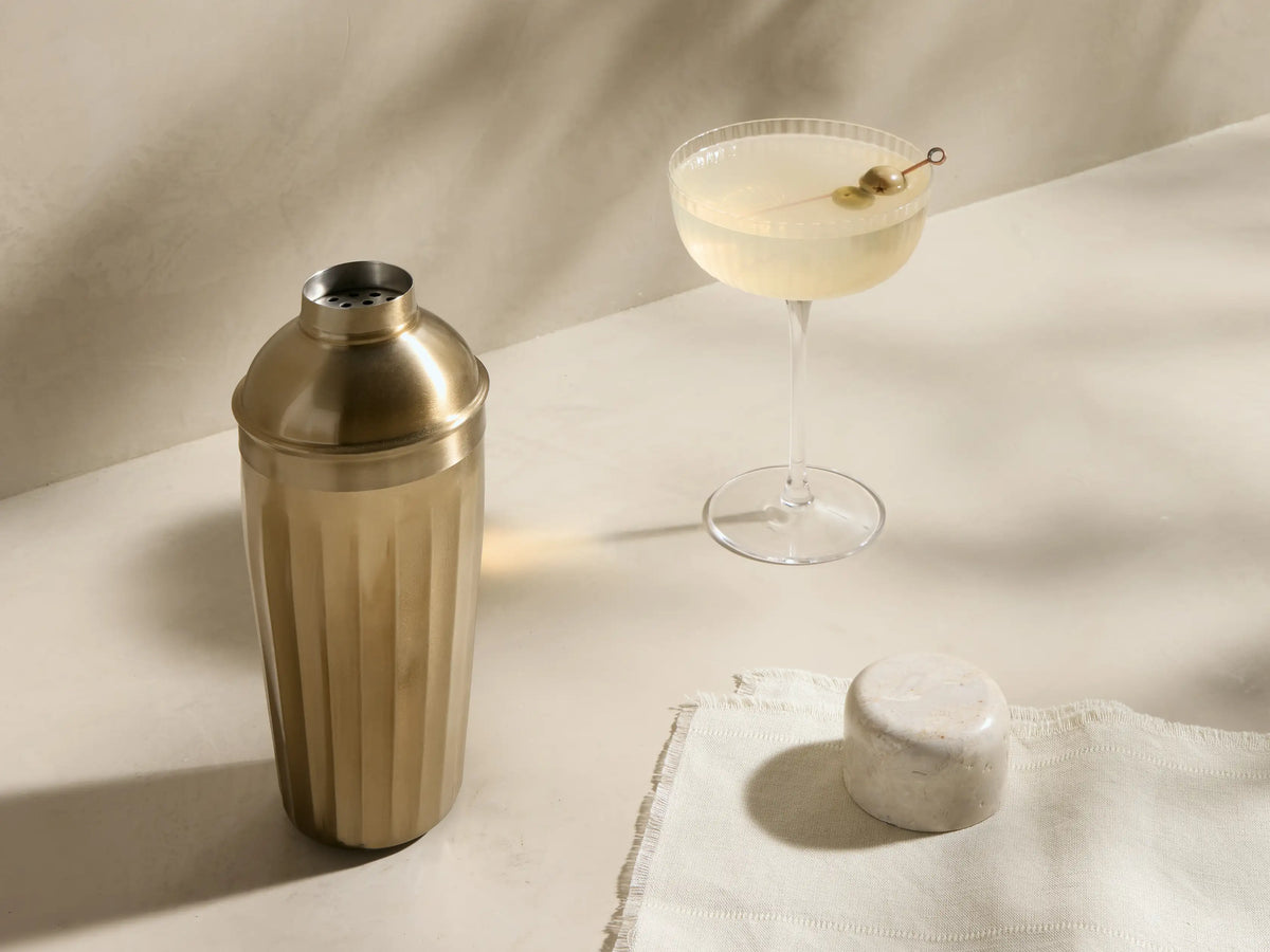 Front view of the Dayana Cocktail Shaker, featuring a light marble cap and a fluted brass-finished body.