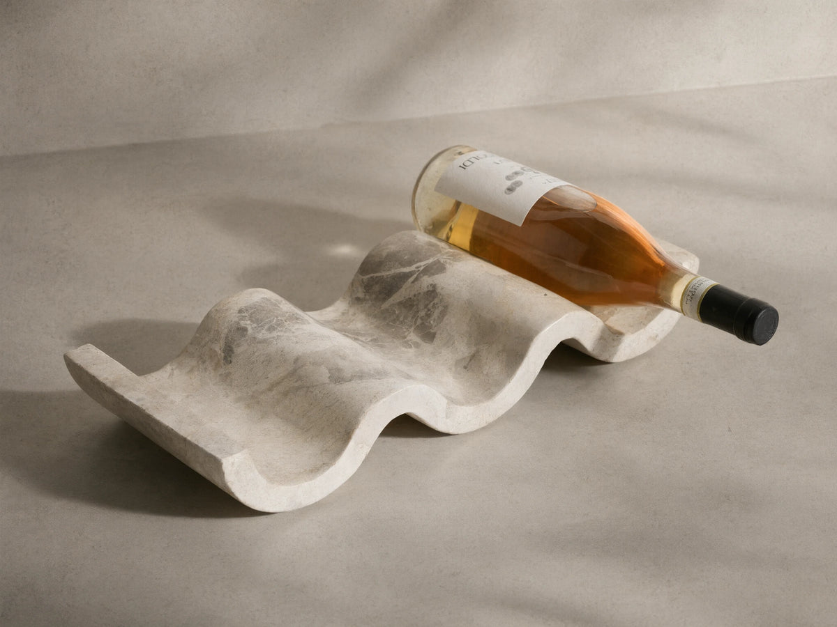 Angled view of the wavy, creamy white Dayana Wine Rack, crafted from natural marble with gray veining, holding a wine bottle.