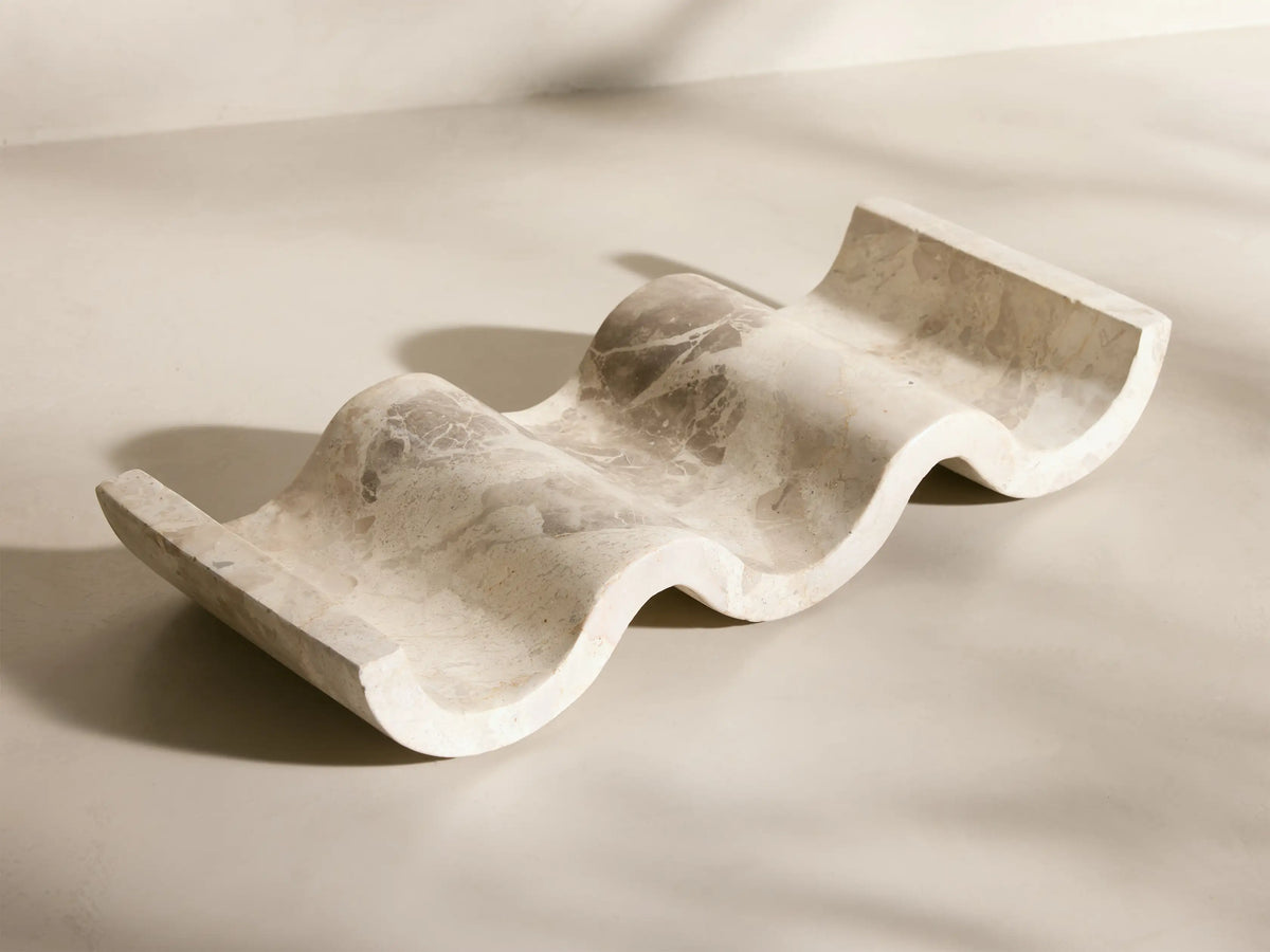 Angled view of the wavy, creamy white Dayana Wine Rack, crafted from natural marble with gray veining, holding a wine bottle.