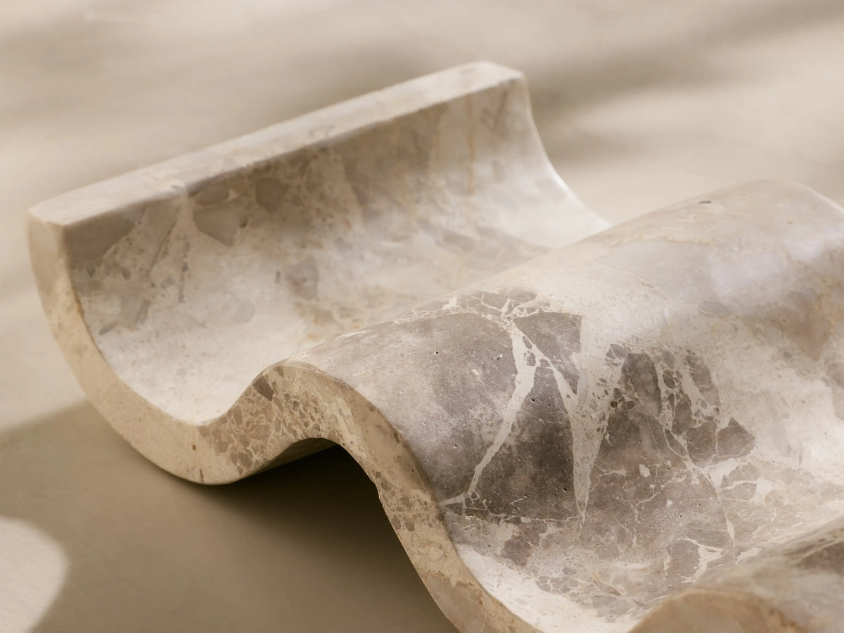 Angled view of the light beige marble Dayana Wine Rack, featuring its undulating design and natural gray veining.