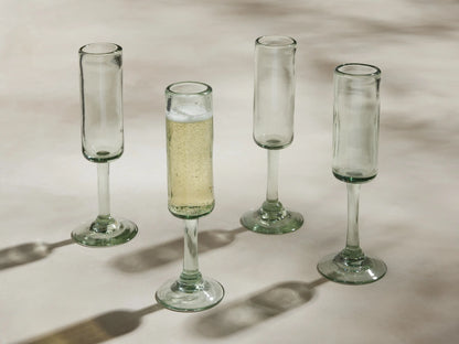 Four handblown Granada Champagne Glasses made from recycled glass. One is filled with champagne, three are empty.