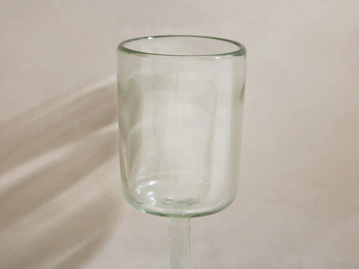 Four Granada recycled glass wine glasses, cylindrical and stemmed. One holds yellow wine, all cast shadows on a light surface.