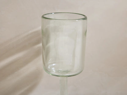 Four Granada recycled glass wine glasses, cylindrical and stemmed. One holds yellow wine, all cast shadows on a light surface.