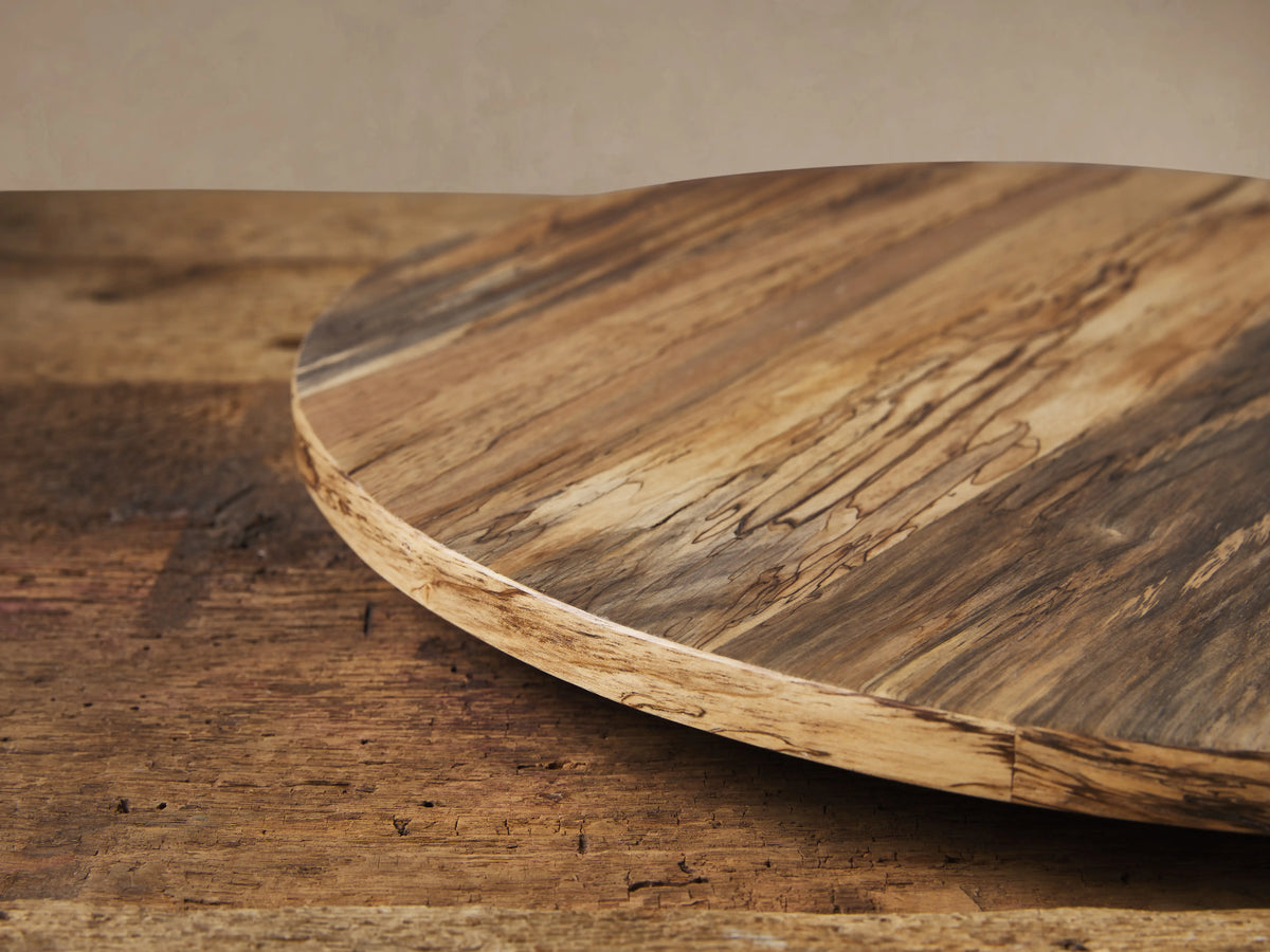 Round Madeira Natural Lazy Susan, crafted from varied light & dark reclaimed wood, rests on a rustic wood table against a beige wall.