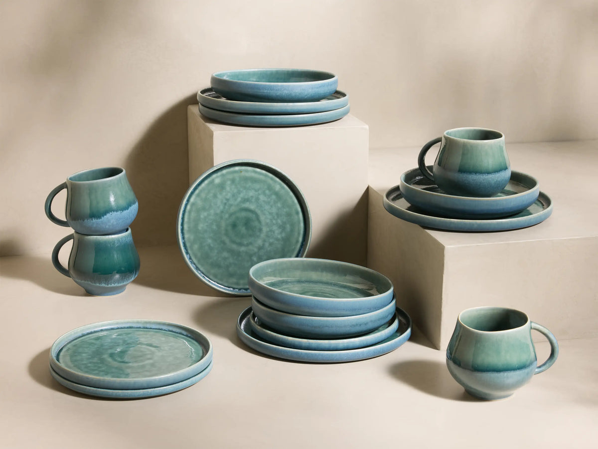 Full set of blue-green reactive glaze Rhoswen Dinnerware With Pasta Bowls, stacked and arranged on different levels.
