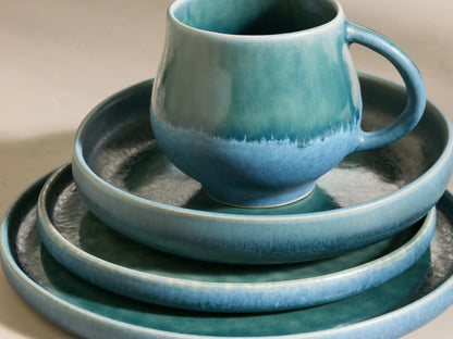 Full set of blue-green reactive glaze Rhoswen Dinnerware With Pasta Bowls, stacked and arranged on different levels.