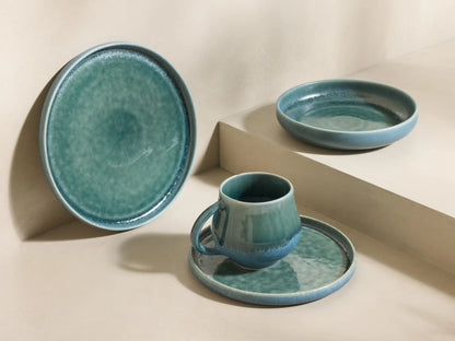 Front view of stacked teal Rhoswen Dinnerware With Pasta Bowls, showcasing reactive glaze on mug, pasta bowl, and plates.