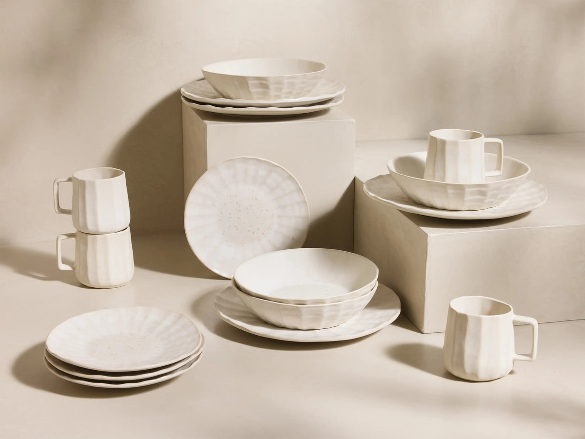 Full set of cream Saskia Dinnerware With Pasta Bowls (Set of 16) with fluted texture, displayed on light risers.