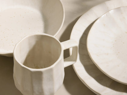 Full set of cream Saskia Dinnerware With Pasta Bowls (Set of 16) with fluted texture, displayed on light risers.