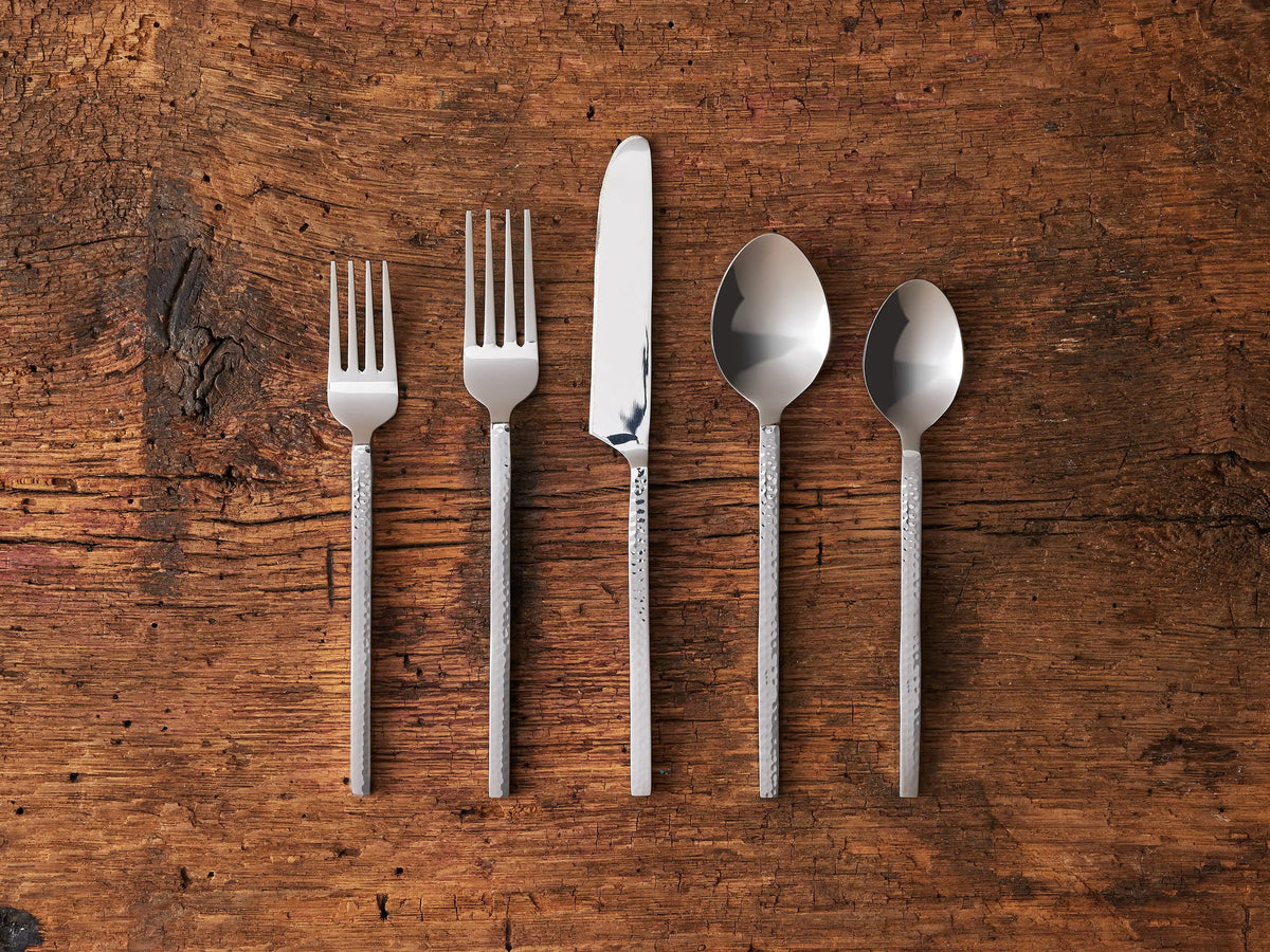 Sethian Five Piece Place Setting on wood surface, featuring modern flatware with square hammered handles; includes fork, knife, spoon.