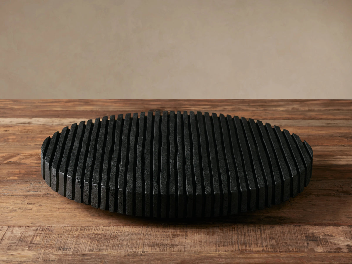 Oval black Slat Lazy Susan made of textured vertical reclaimed wood slats, resting on a rustic wooden table.