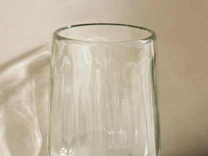 Four ribbed Seema Clear Goblet Glasses with a green tint. One glass in front holds a yellow drink with ice & lemon slice.