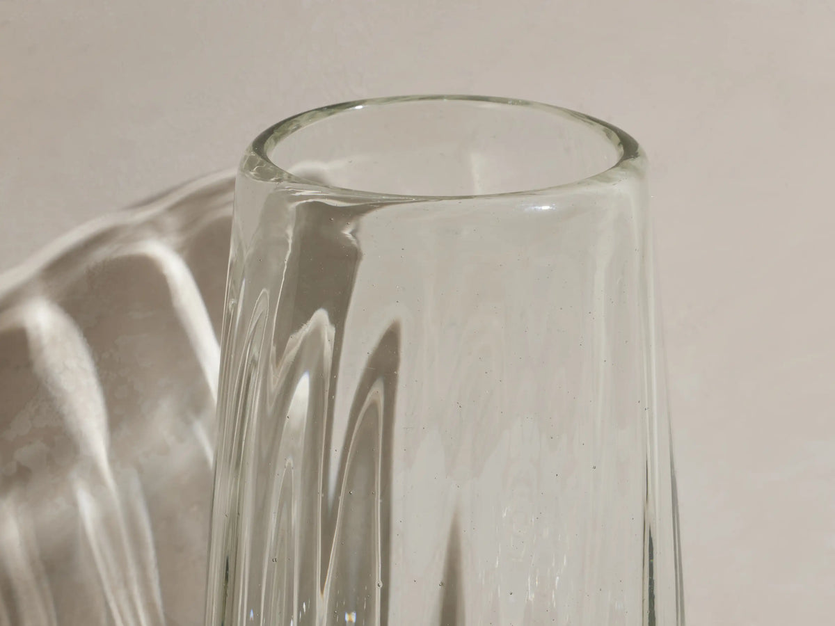 Seema clear highball glasses, set of 4. One glass contains iced amber drink with lemon & stirrer. Textured, recycled glass.