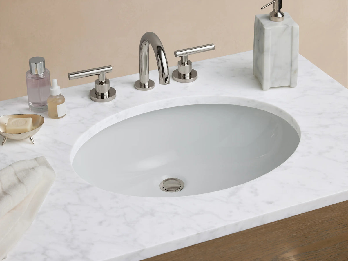 Calista Double Vanity in oak wood with six drawers and silver handles, stone top with two sink spaces, set against a neutral wall.