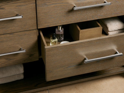 Open drawer of the Calista Double Vanity made of oak wood, showing folded white towels and a bottle. Carrara marble top visible above.