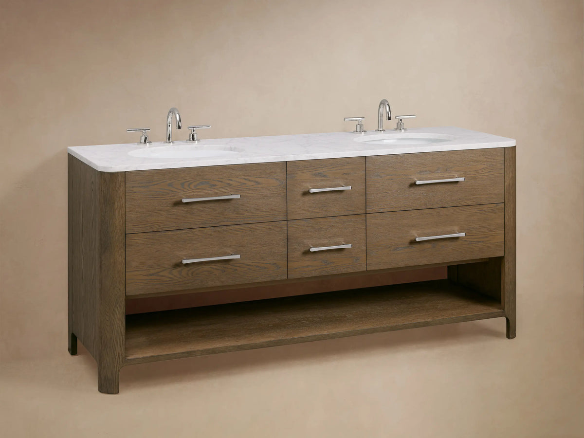 An open oak wood drawer of the Calista Double Vanity showing interior storage, with metal handles, toiletries, and neatly folded towels.