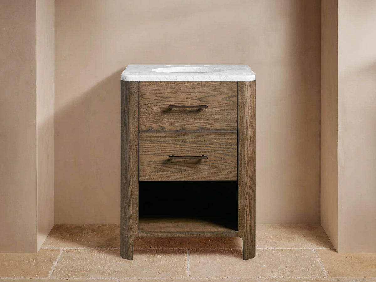 Calista Powder Vanity. Dark oak wood vanity with white marble top, two drawers, open shelf with towels, dark bronze faucet.