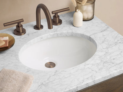 Dark brown oak Calista Powder Vanity with white marble top, oval sink, 2 drawers with black pulls, and open shelf.
