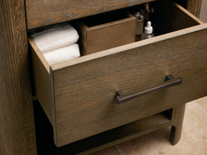 Calista Powder Vanity, white oval sink, veined marble countertop, bronze faucet, soap, towel, and jar of cotton balls.