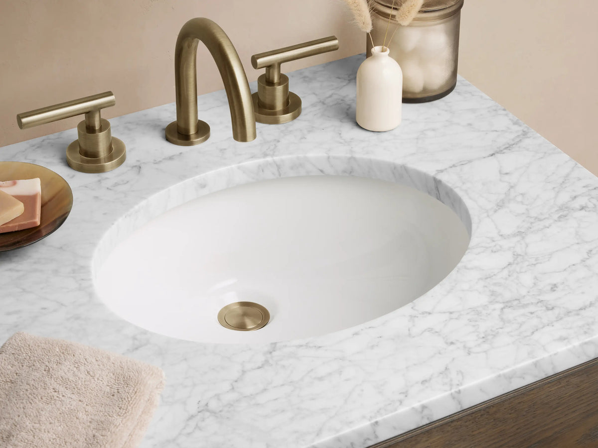 Calista Powder Vanity in oak wood with a white marble top, featuring two drawers with brass handles, set against a neutral wall.