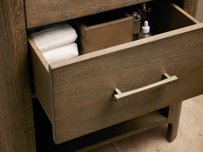 Calista Powder Vanity with a honed marble top, oval ceramic sink, and brass faucet, surrounded by decor items.