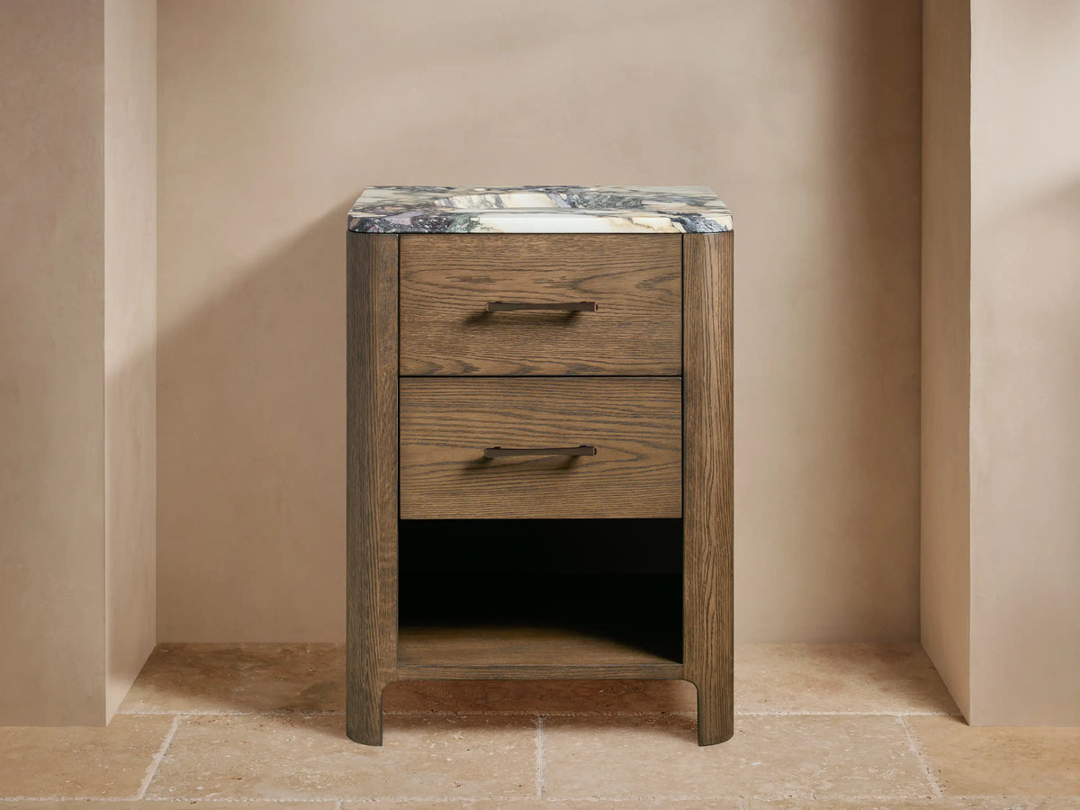 Calista Powder Vanity: Medium brown oak wood vanity with 2 drawers, open shelf, variegated marble top, and bronze faucet.