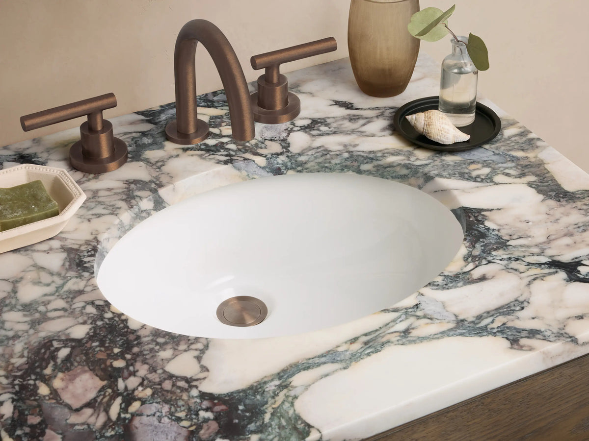 Calista Powder Vanity: Medium brown oak vanity with two drawers, open shelf, and a multicolored marble top, in a room corner.