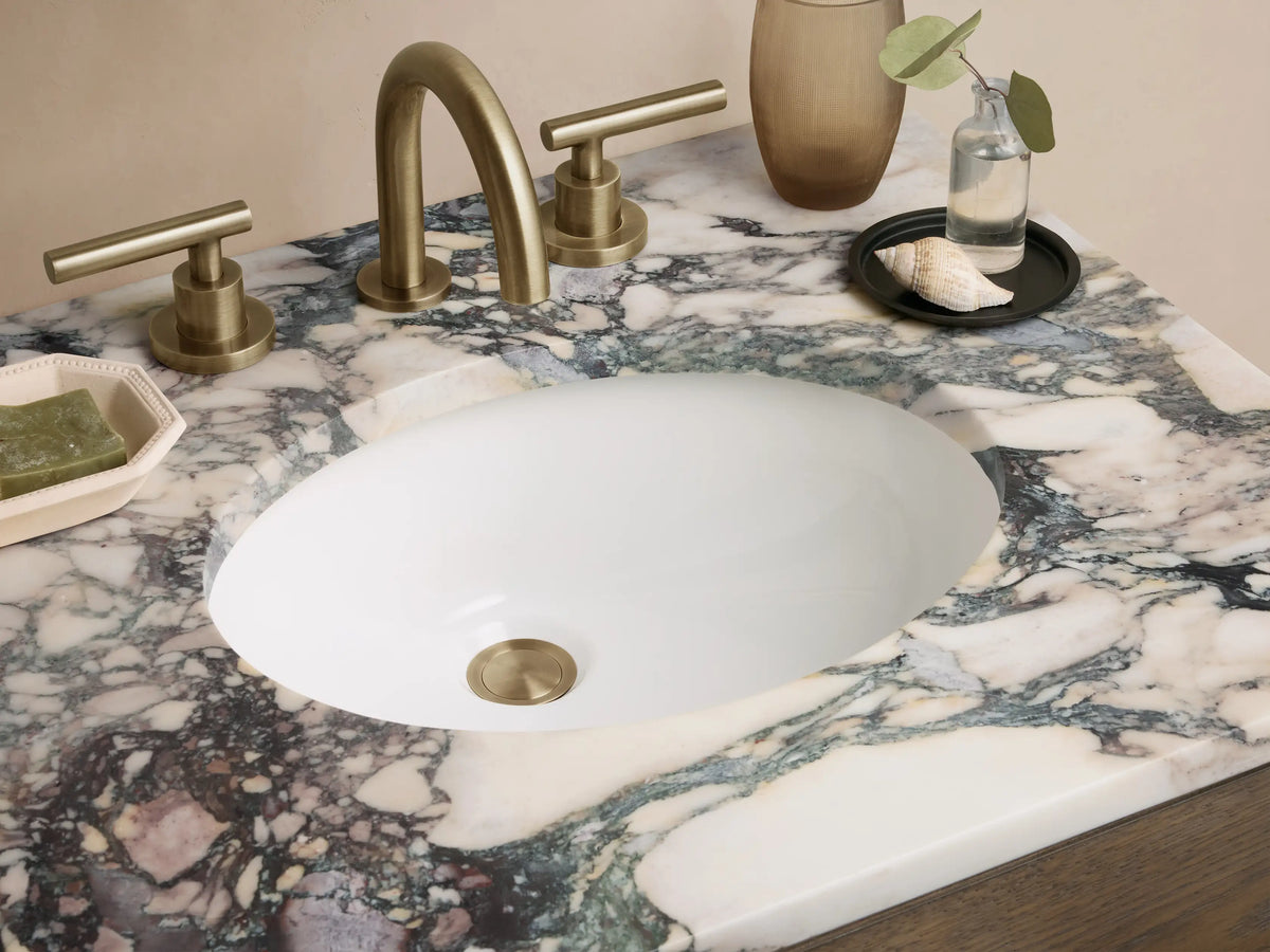 Calista Powder Vanity with oak wood finish, two drawers, marble stone top, and metal handles, placed on a tiled floor.