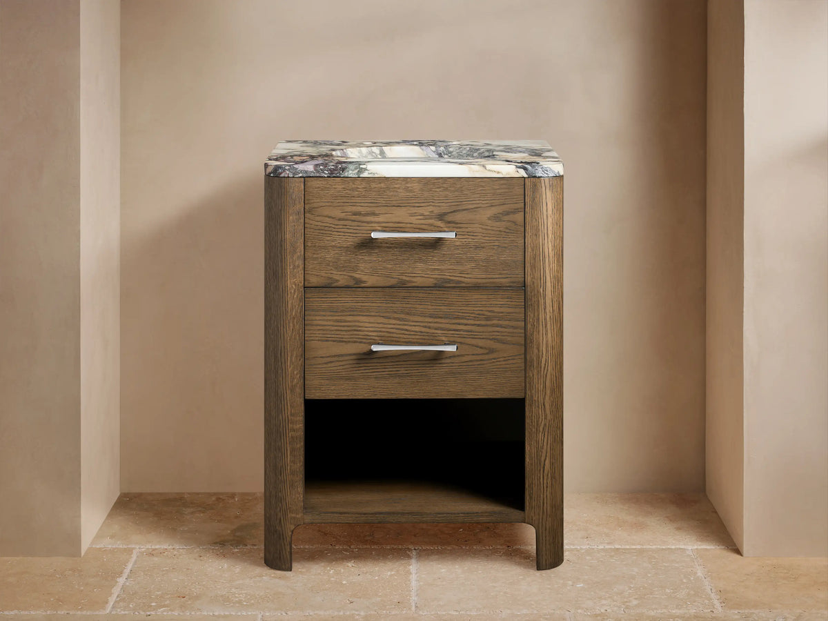 Calista Powder Vanity: Medium brown oak wood vanity with veined marble top, chrome faucet, 2 drawers, open shelf on tiled floor.