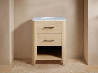 Calista Powder Vanity: Light oak wood vanity with white marble top, oval sink, dark faucet, 2 drawers with bronze pulls, open shelf.