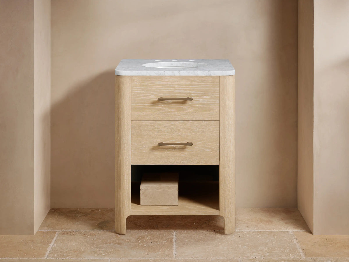 Calista Powder Vanity with light oak finish, topped with Carrara or Calacatta Viola marble. Features brass hardware, marble backsplash.