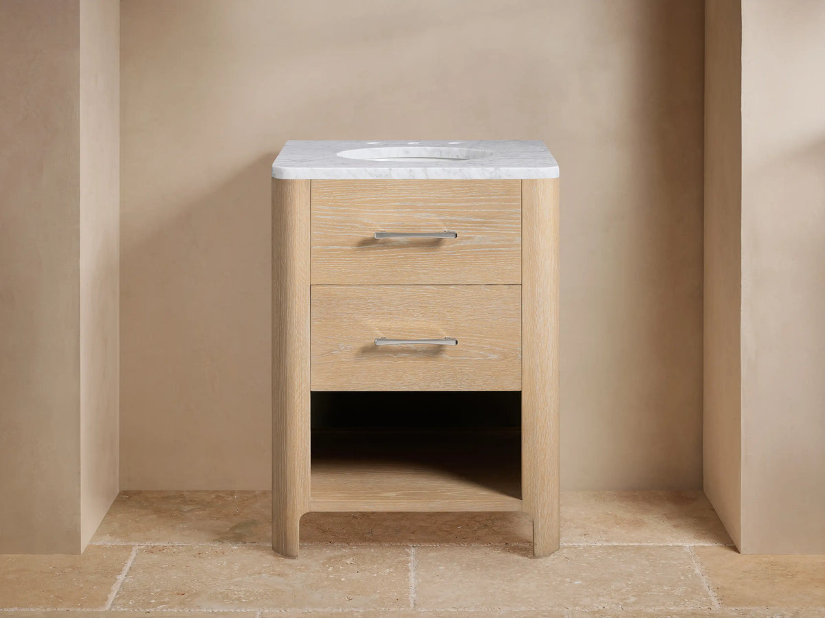 Calista Powder Vanity with light wood finish, two drawers, marble top, oval sink, silver hardware, staged against beige walls.