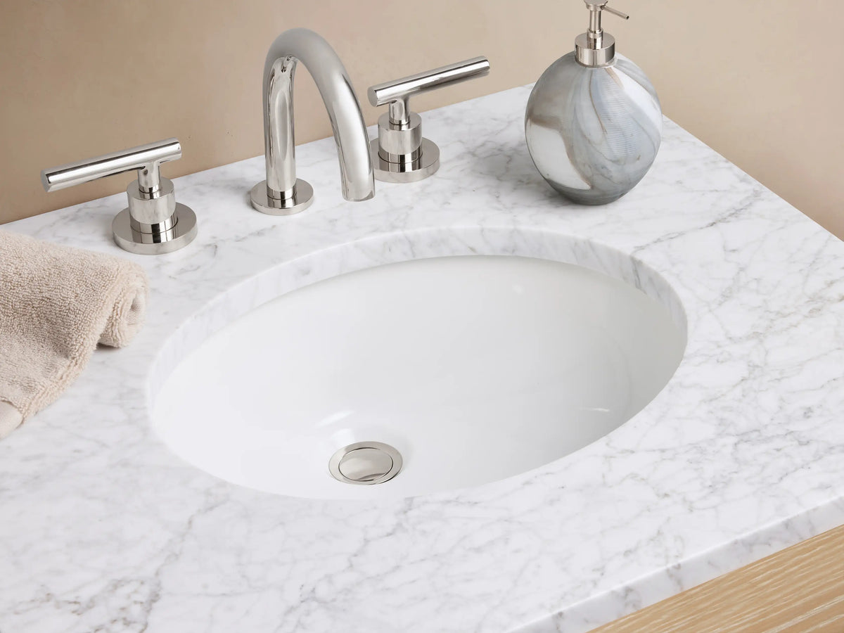 Calista Powder Vanity with oak wood finish, marble stone top, two drawers, and an open shelf underneath, placed against a beige wall.