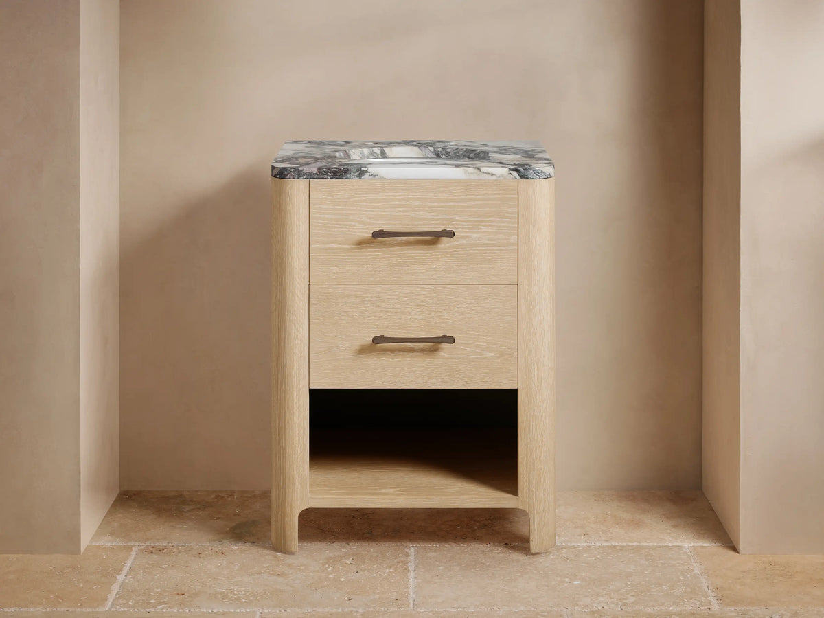 Calista Powder Vanity: Light oak wood vanity, dark veined marble top, two drawers, open shelf, dark faucet, & soap dispenser.