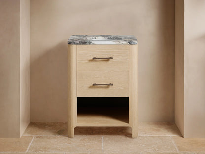 Calista Powder Vanity: Light oak wood vanity, dark veined marble top, two drawers, open shelf, dark faucet, & soap dispenser.
