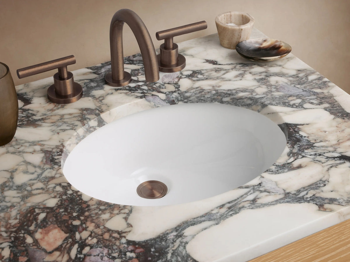 Calista Powder Vanity: light oak wood, mottled marble top, two dark-handled drawers, open shelf, against light walls.