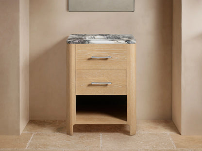 Calista Powder Vanity with oak wood finish, two drawers, and a black and white marble top. Sink with rolled towels beneath.