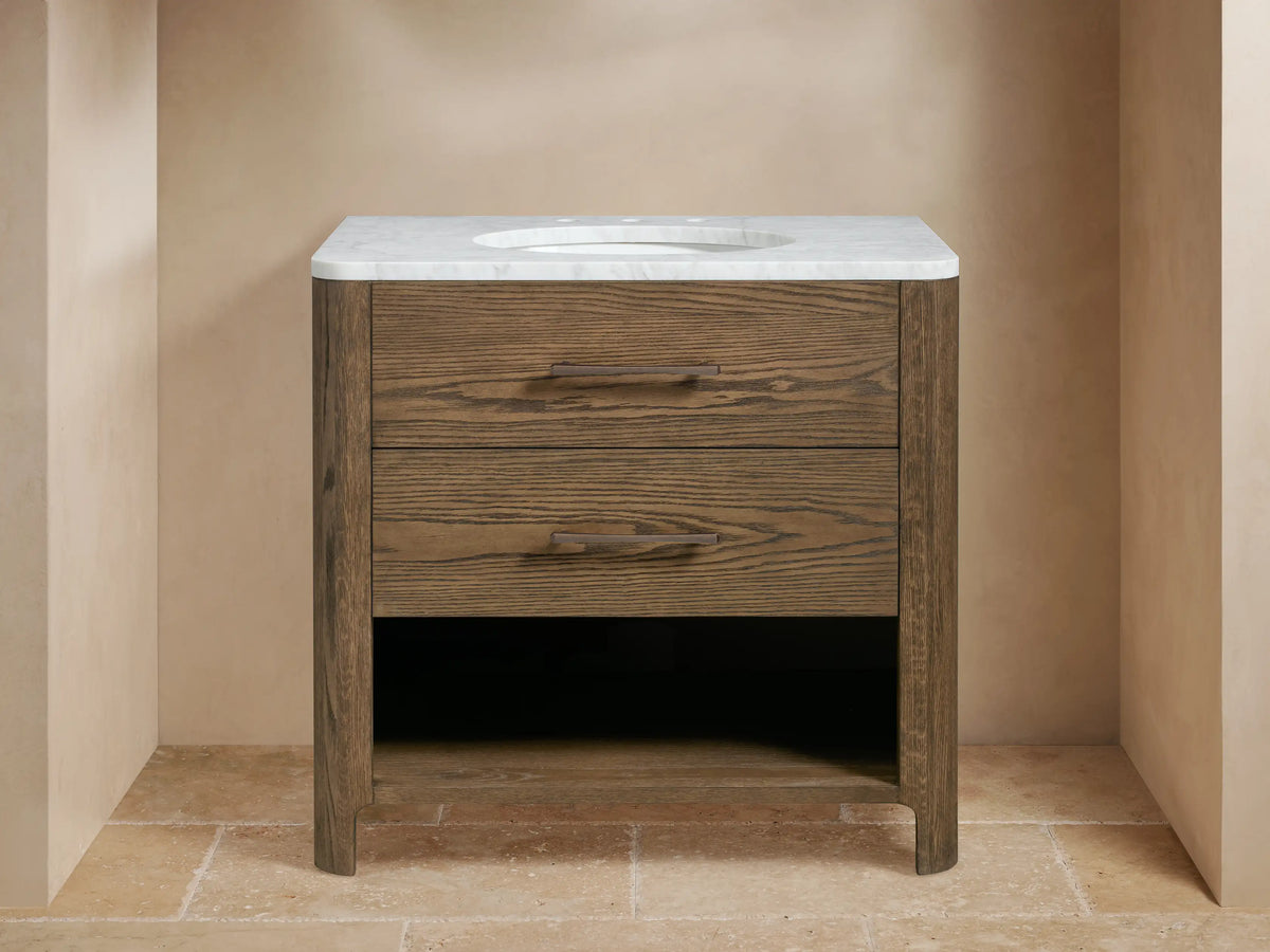 Calista Single Vanity: dark oak wood with white marble top, undermount sink, bronze faucet, two drawers, open shelf.