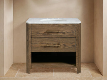 Calista Single Vanity in oak wood with two faux drawers, Carrara marble top, oval sink, brass hardware, and open shelf below.