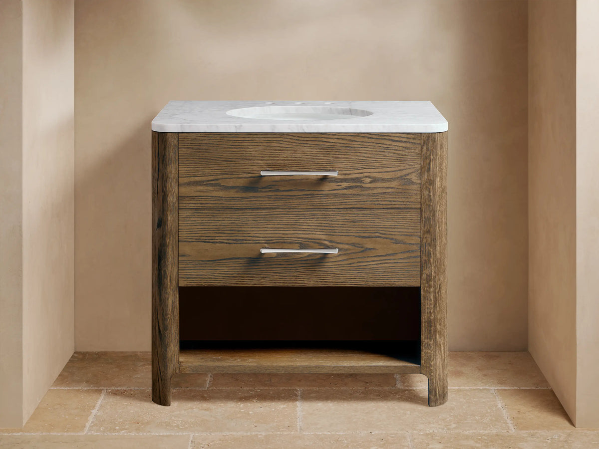 Calista Single Vanity with oak wood finish, two drawers with metal handles, stone top, and oval undermount sink, staged in a bathroom setting.
