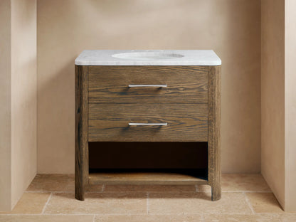 Calista Single Vanity with oak wood finish, two drawers with metal handles, stone top, and oval undermount sink, staged in a bathroom setting.