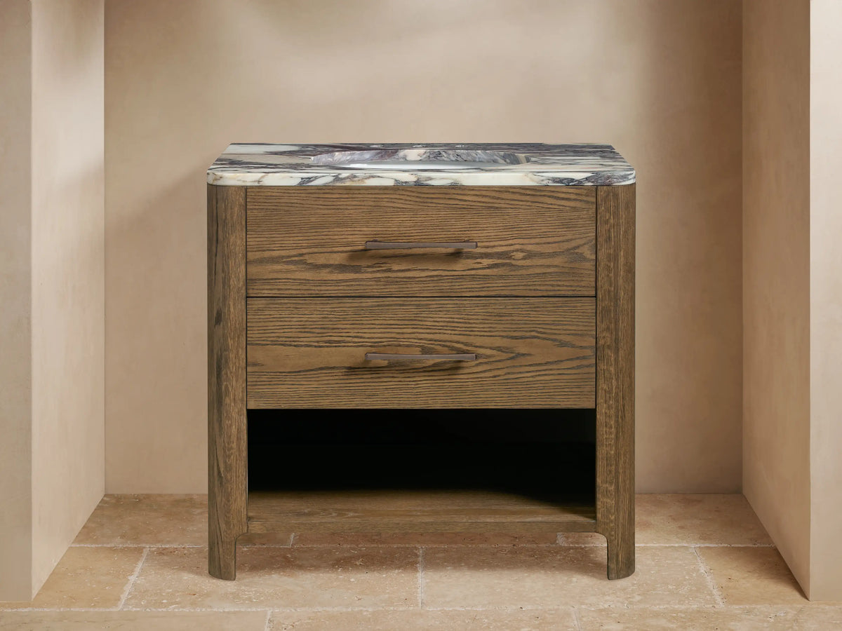 Calista Single Vanity in medium brown oak finish with gray veined marble top, two drawers, and open shelf holding white towels.