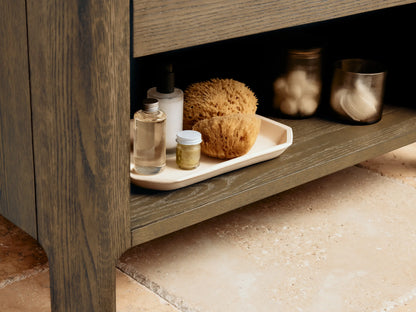 Open drawer of the Calista Single Vanity in oak wood with metal handles, displaying a soap dish, essential oil bottle, and storage box on a wood-textured surface.