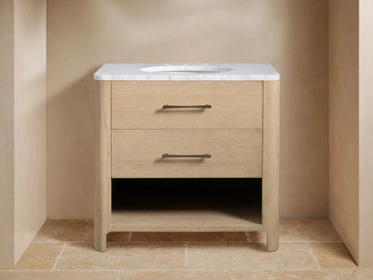 Calista Single Vanity. Light oak wood vanity with white marble top, undermount sink, bronze faucet, two drawers & open shelf with towels.