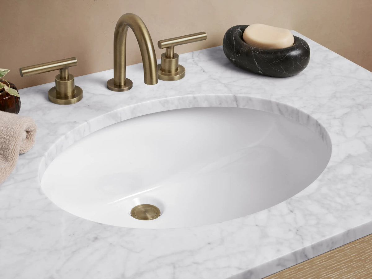 Calista Single Vanity with light oak wood finish, two drawers, silver handles, and a white marble stone top with an oval sink.