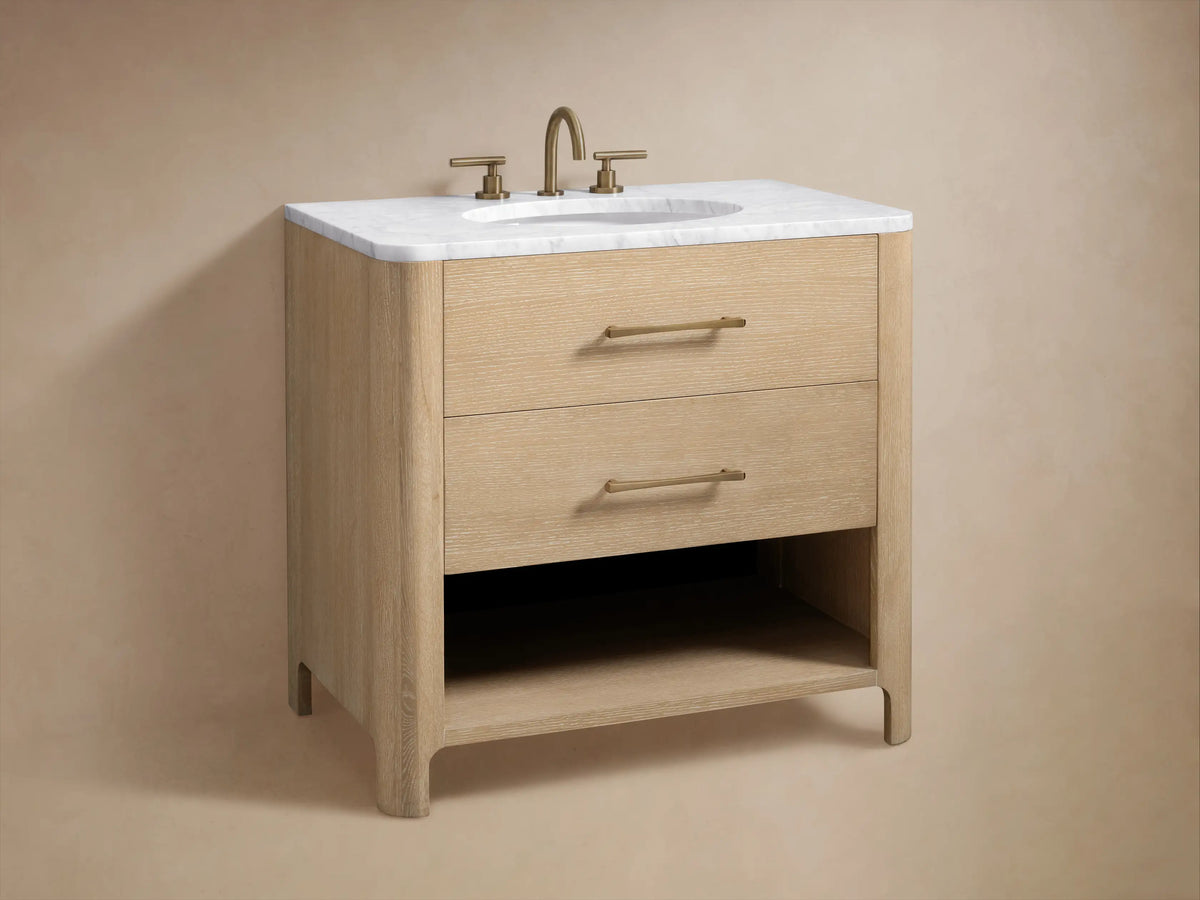 Calista Single Vanity open drawer with brass handle shows bottles and towels on a light oak finish against a stone floor.