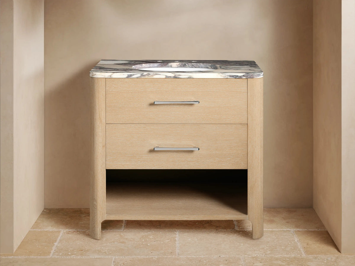 Calista Single Vanity with oak wood finish, marble stone top, ceramic sink, dual silver handles, open shelf with towels.